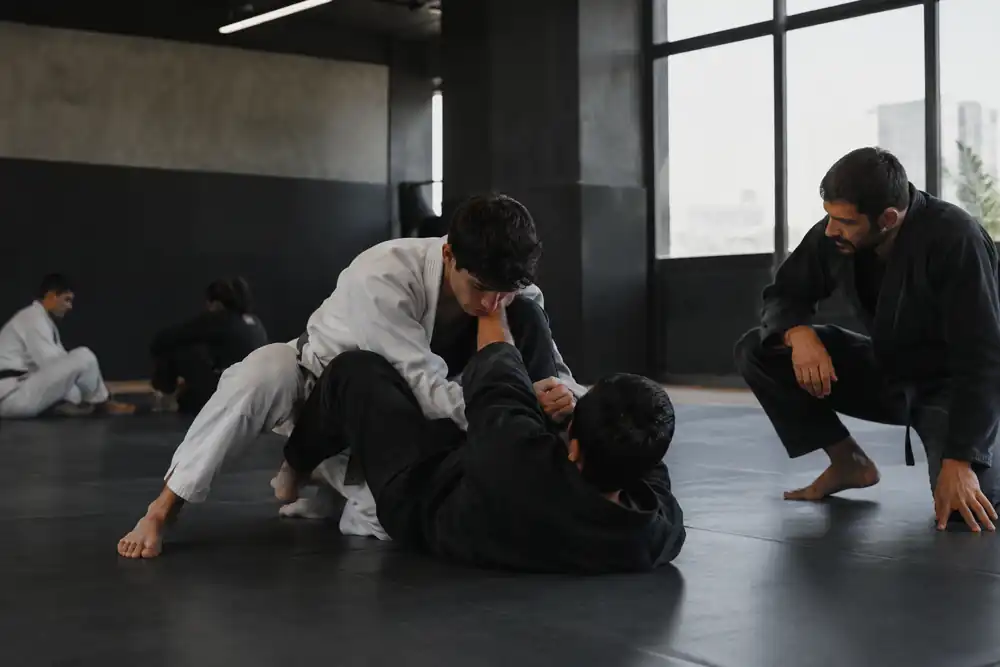 Professor acompanhando dois alunos treinando jiu-jitsu no tatame