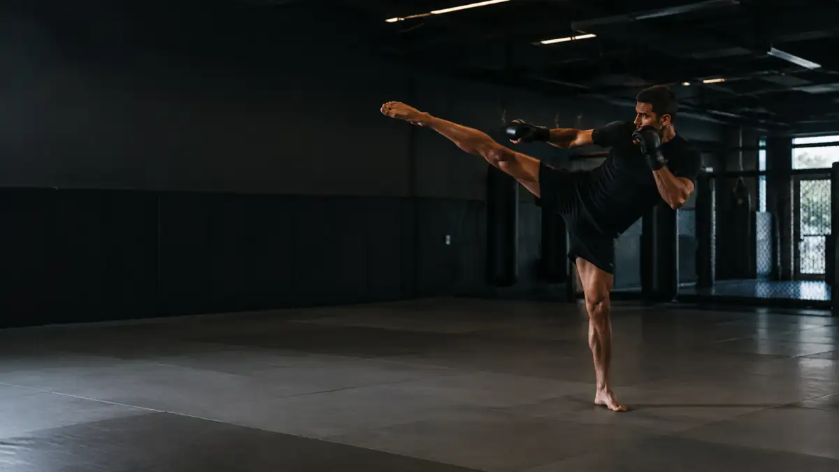 Atleta de muay thai dando um chute alto no tatame